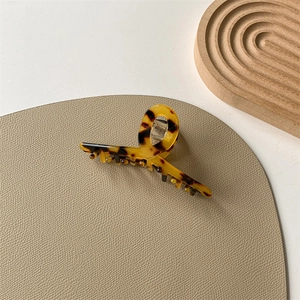 Detail of tortoiseshell leopard print acetate hair claw clip with metal spring on beige pad