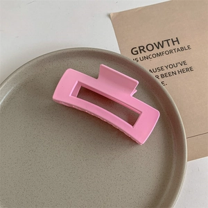 Macro detail of a matte pink rectangular claw clip with a hollow design on a ceramic plate