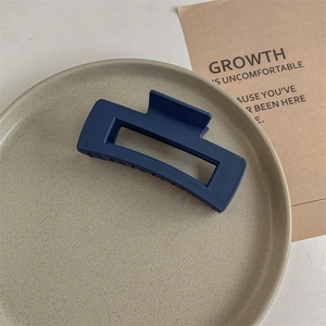 Close-up of matte navy blue rectangular claw clip on a gray ceramic plate