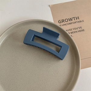 Macro view of a matte navy blue rectangular hair claw clip on a minimal beige tray