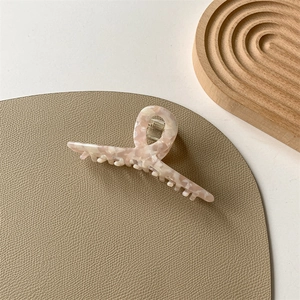 Detail of French acetate hair claw clip with pink marble texture on leather and wood