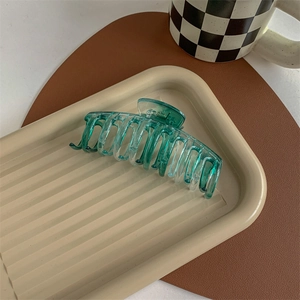 Close-up of translucent cyan hair claw clip with durable metal spring on a tray