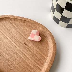 Close-up of pink checkered heart hair claw clip on a wooden tray with aesthetic props