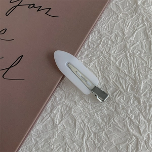 Close-up of white candy-colored hair clip with silver metal base on textured paper