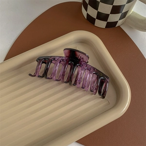 Macro view of a large translucent deep purple shark hair claw clip on a modern tray