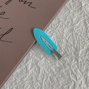 Detail view of a matte sky blue hair clip with a stainless steel base on a white texture