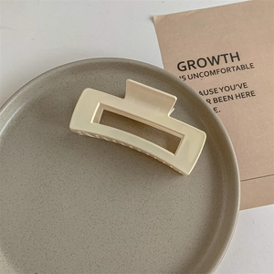Detail of a large matte cream square claw clip on a textured grey background