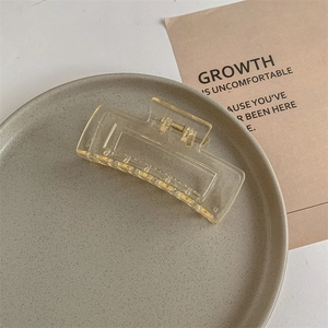 Close-up of amber yellow square claw clip with golden spring on ceramic tray