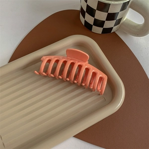 Close-up of matte coral orange hair claw clip on a decorative tray with aesthetic setup
