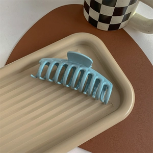 Macro detail of the light blue matte hair claw clip on a decorative striped tray