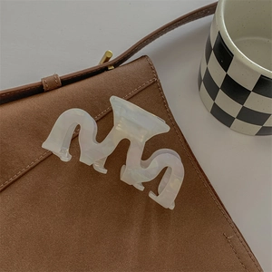 Detail shot of a large wavy pearl white acetate shark hair claw on a brown bag