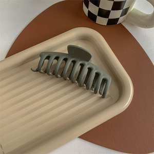 Close-up of a large matte olive green shark hair claw clip on a vintage aesthetic tray