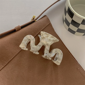 Detail of large acetate hair claw with cream marble pattern and wavy wave edge design