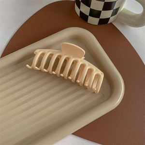 Close-up of large matte cream shark hair claw clip on an elegant wavy ceramic tray
