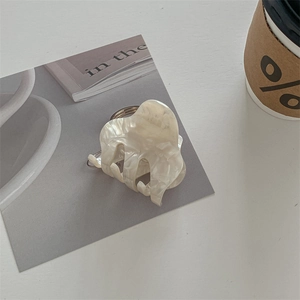 Detail of a white marble acetate hair claw clip with shell luster texture on a minimal card