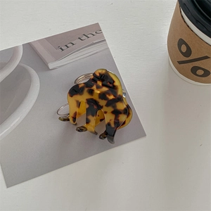Detail view of tortoiseshell resin hair claw clip with silver spring on a minimal desk