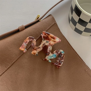 Macro detail of marble pattern acetate hair claw on brown suede bag with warm lighting