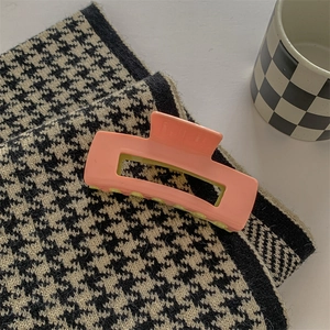 Macro detail of glossy pink acetate rectangle hair claw clip on houndstooth fabric