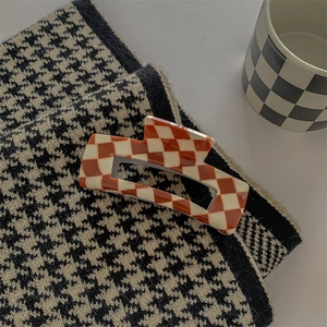Detail of orange checkered acetate hair claw clip on houndstooth fabric background