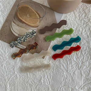 Chic wavy acrylic hair clips in tortoise shell and solid colors on a white fabric background