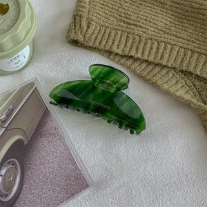 Detail view of handmade emerald green marble acetate hair claw clip with golden lettering