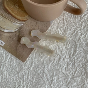 Detail of wavy acetate hair clips in pearlescent cream white on a textured background