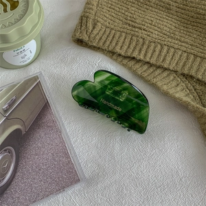 Detail of dark green marble hair claw clip with golden handmade lettering on soft fabric