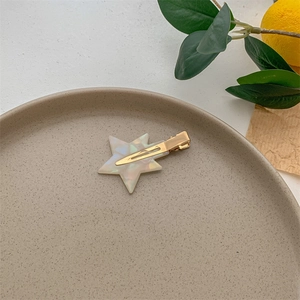 Close-up of a pearlescent star-shaped acetate hair clip on a ceramic tray with citrus
