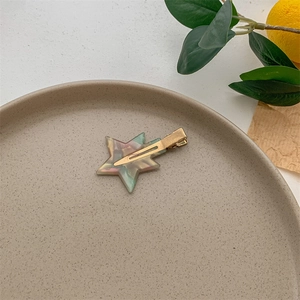 Detail view of starry acetate hair clip with golden duckbill clasp on ceramic tray