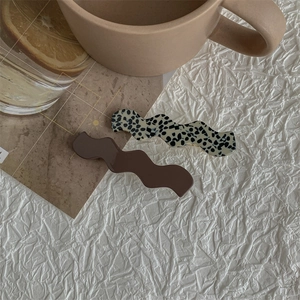 Detail of wavy resin hair clips set in dark coffee and dalmatian print on white fabric