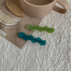 Detail view of green and teal wave-shaped hair clips on a textured white surface