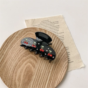 Detailed close-up of a black hair claw clip with red cherry rhinestones on a wooden tray