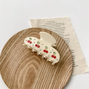 Detail view of cream hair claw with red rhinestone cherry pattern on a wooden tray