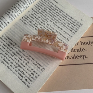 Detailed close-up of a large pink acetate hair claw clip on a minimalist book background