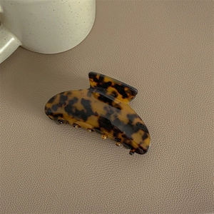 Close-up of large tortoiseshell hair claw clip on leather surface with ceramic cup