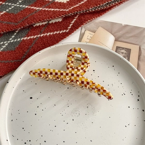 Close-up of yellow and white checkered acetate hair claw clip on a stylish fabric background
