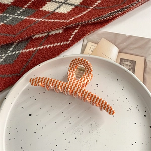 Close-up of a large orange houndstooth hair claw clip on a stylish ceramic plate