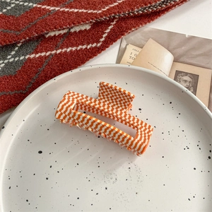 Macro detail of an orange checkered acetate hair claw clip on a decorative white plate