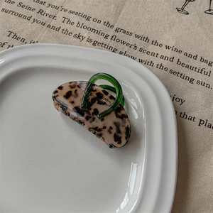 Détail d'une pince à cheveux écaille avec poignée vert foncé sur plat en céramique
