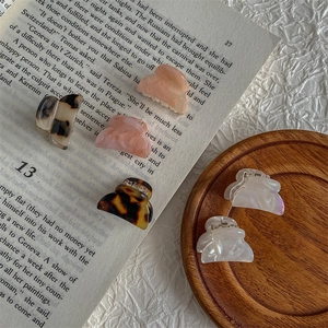 Mini acetate hair claws in tortoise shell and pink marble patterns on a wooden tray