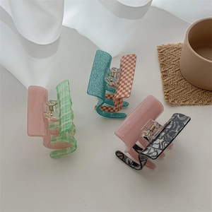 Pink and green checkerboard acetate hair claw clips in a minimalist lifestyle setting