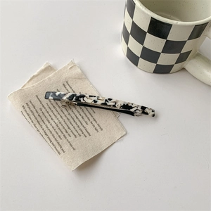 Détail d'une pince à cheveux rectangulaire à motif vache noir et blanc sur lin beige
