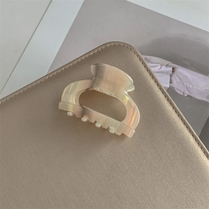 Dettaglio del fermaglio per capelli in acetato color crema su una borsa in pelle marrone