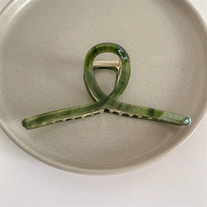 Detalle de pinza para el pelo en acetato verde mármol con diseño cruzado elegante
