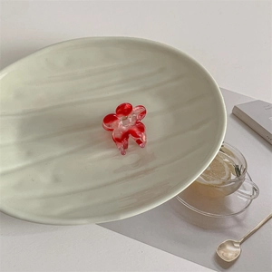 Macro shot of red floral acetate hair claw on a ceramic plate for a sweet aesthetic look