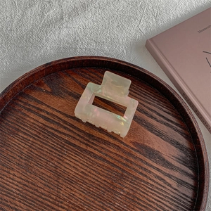 Macro view of rectangular iridescent pink acetate hair claw clip on wooden tray