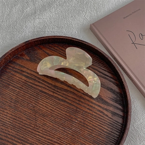 Macro shot of French style acetate hair claw clip with pearlescent finish on wooden tray