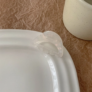 Détail macro d'une pince à cheveux blanc crème avec texture nacre sur un bord en céramique