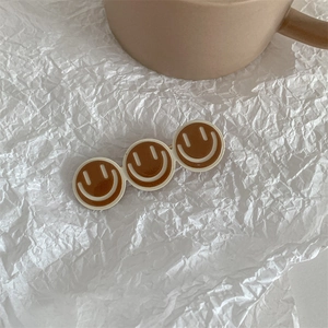Detail view of cute smiley face hair clip featuring brown and cream yellow accents