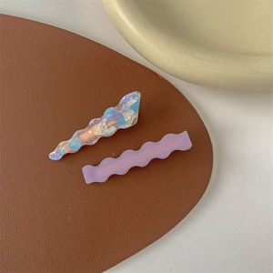 Close-up of wavy marbled acetic acid and purple hair clips on brown leather texture